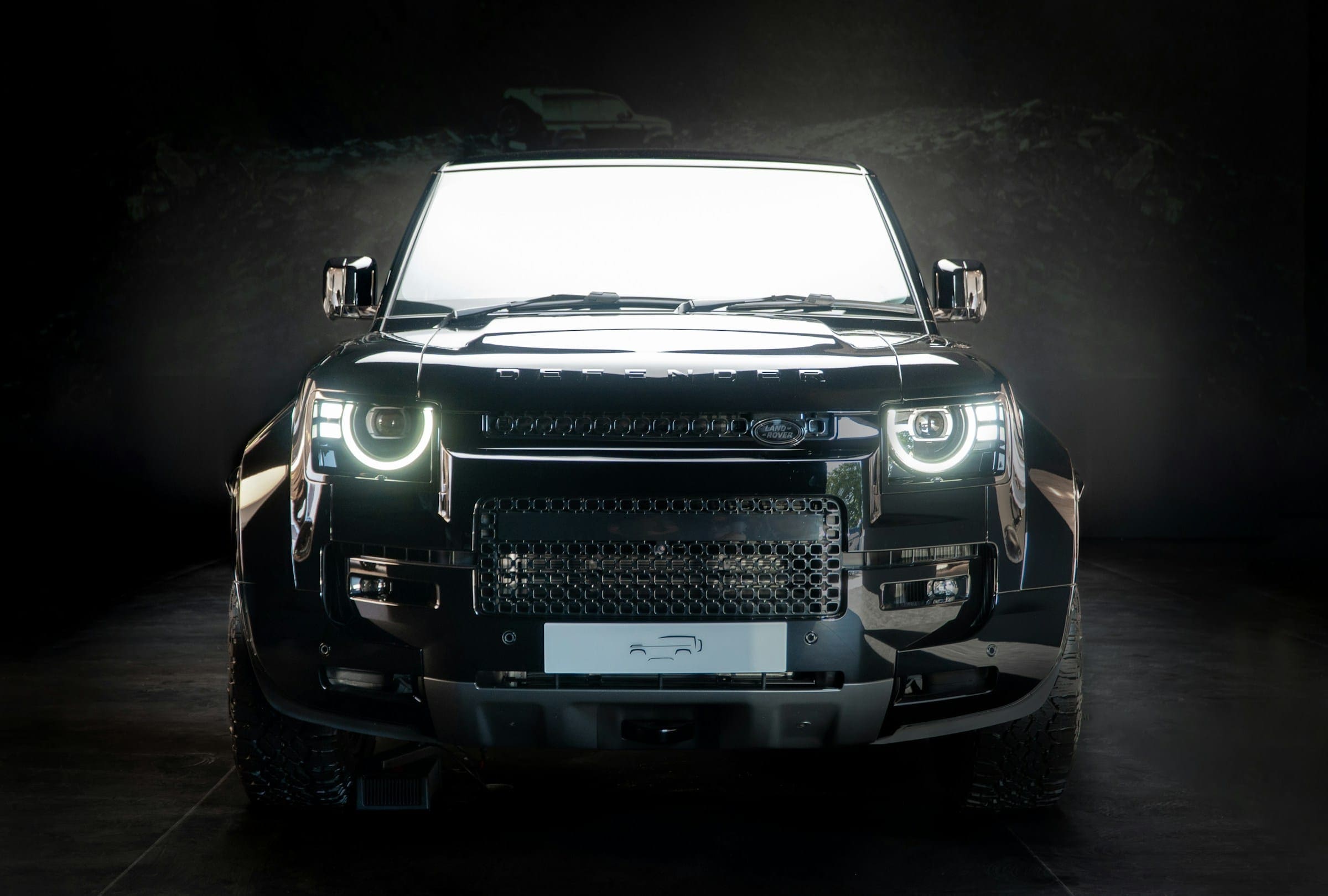 Black Land Rover Defender in a dark studio with its LED headlights on